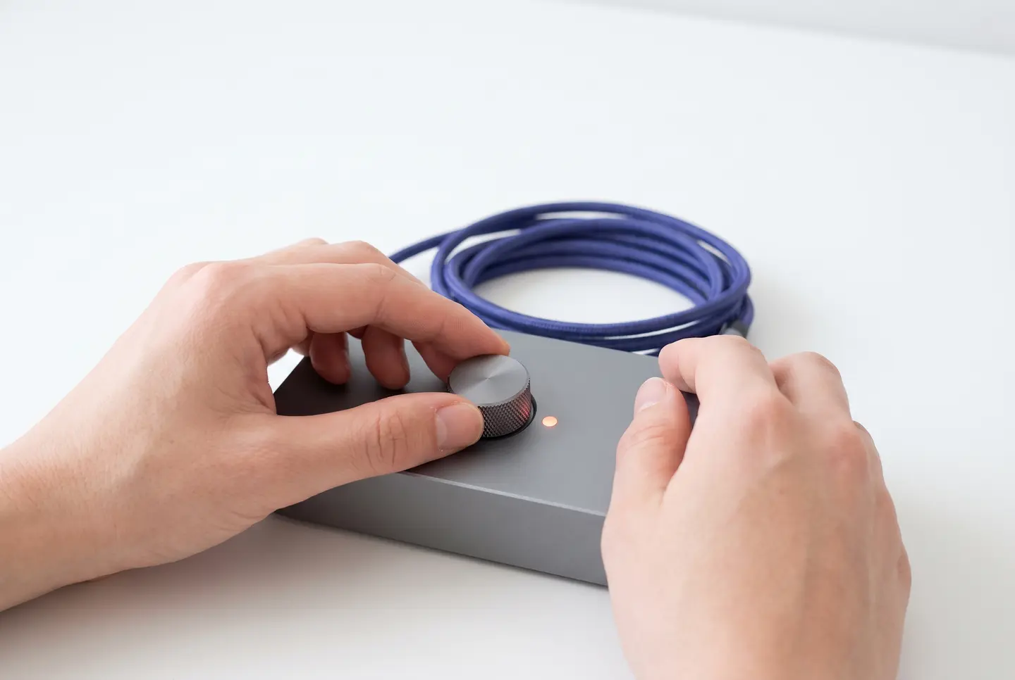 Hands turning the gain knob on a compact audio interface beside a glowing signal light
